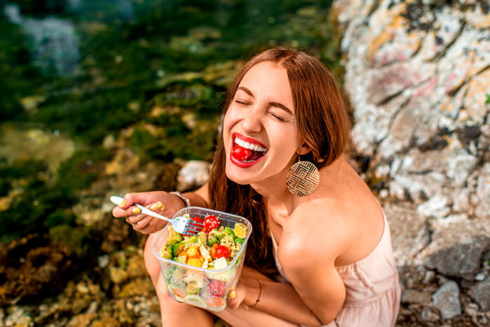mulher de cabelos castanhos e compridos comendo salada com tomates.