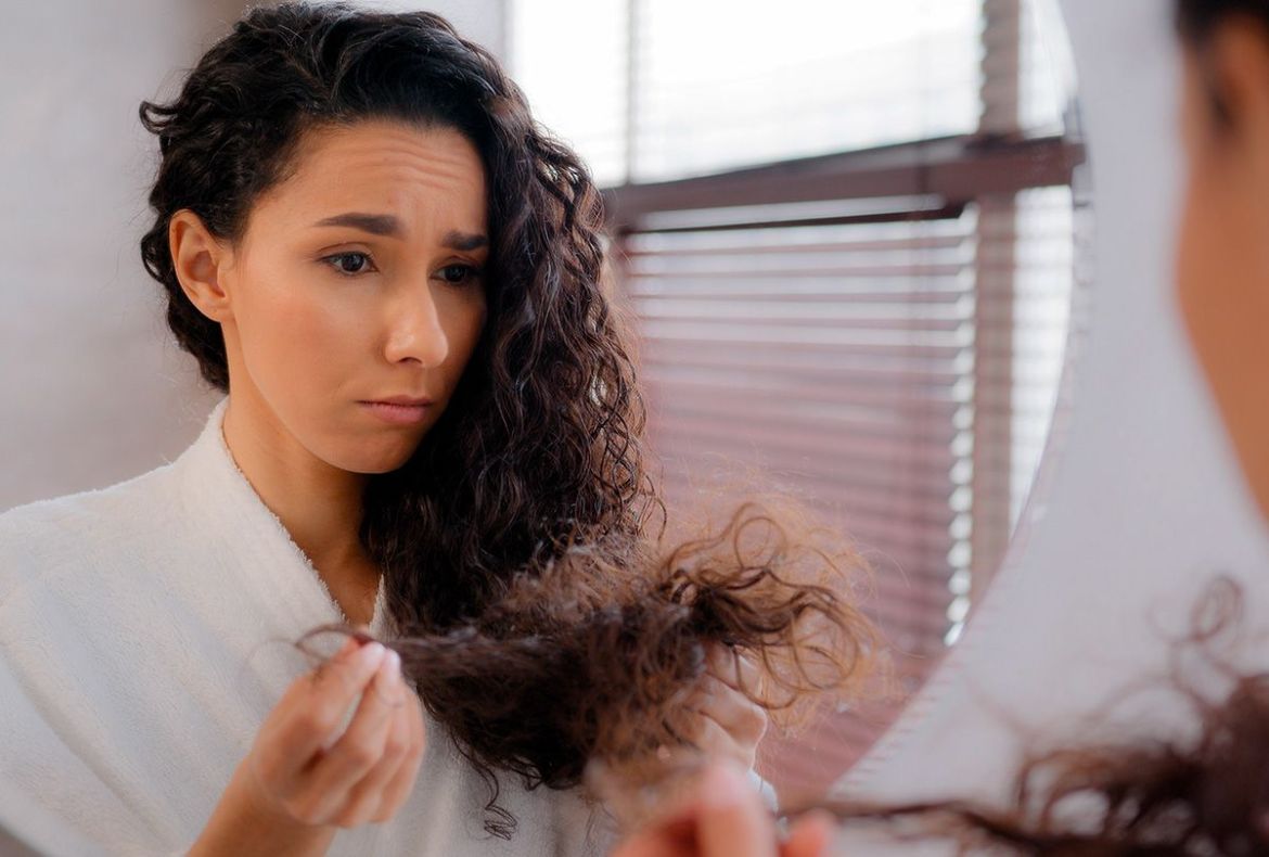 mulher com o cabelo ondulado, em frente ao espelho, olhando para as pontas do cabelo seco: o que fazer?